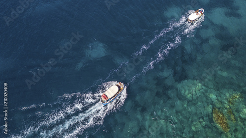 Aerial view of two white motorboats running on the azure waters of the Tyrrhenian Sea. On his trip near the coast the boat leaves a white trail in the waves of the sea.