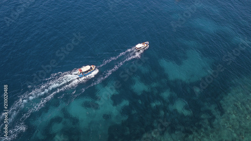 Aerial view of two white motorboats running on the azure waters of the Tyrrhenian Sea. On his trip near the coast the boat leaves a white trail in the waves of the sea.