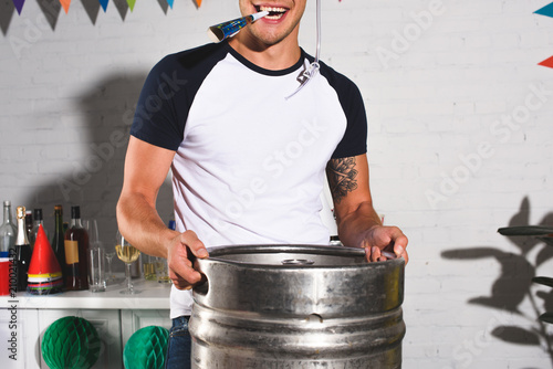 Φωτογραφία cropped shot of happy young man holding barrel of beer at home party