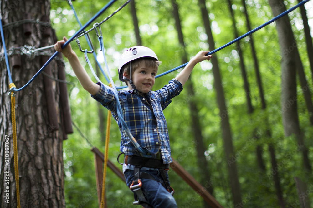 boy enjoys climbing in the ropes course adventure. smiling child engaged climbing high wire park.