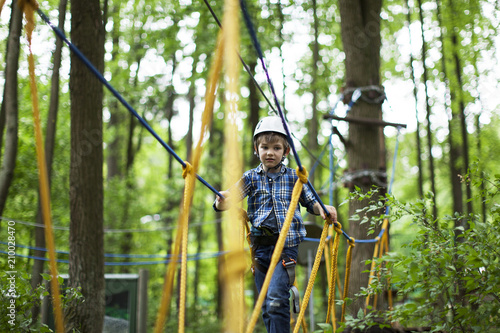 boy enjoys climbing in the ropes course adventure. smiling child engaged climbing high wire park.