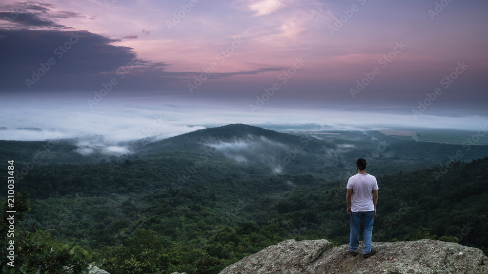 Man standing on the rock and watching hill surrounded with fog