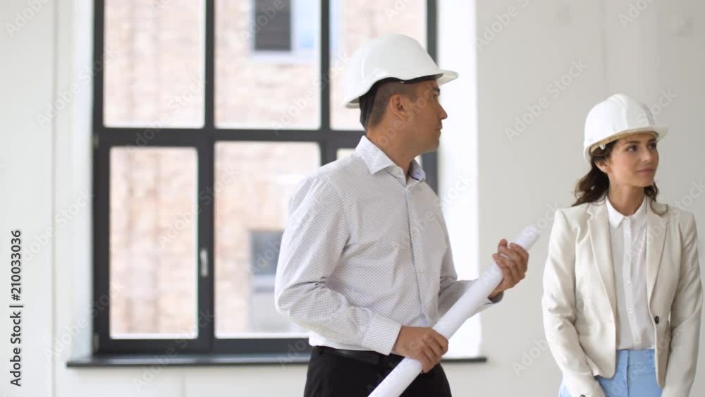 architecture, construction business and people concept - architect or realtor showing new office room to customers with blueprint and helmets architecture, construction business and people concept - architect or realtor showing new office room to customers with blueprint and helmets