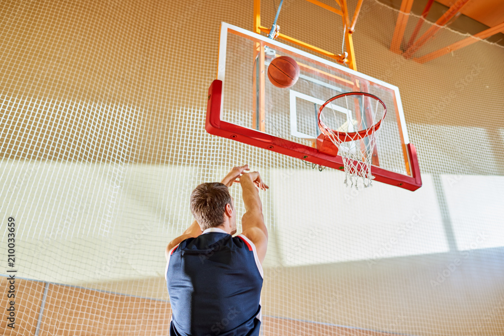 Fototapeta premium Back view of faceless man in basketball uniform shooting goal while playing in gym. 