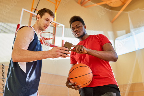 Two basketball players standing on court in gym and browsing smartphone together.  © Seventyfour