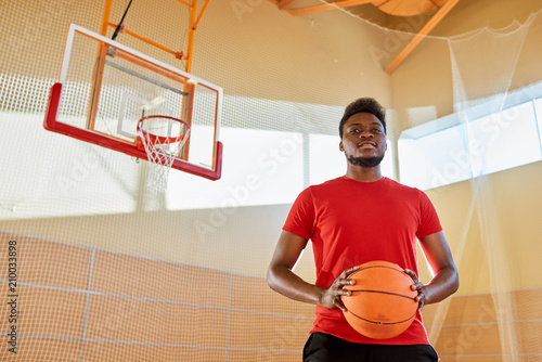 Attractive African-American basketball player with ball smiling and looking at camera while standing on court in gym.  © Seventyfour