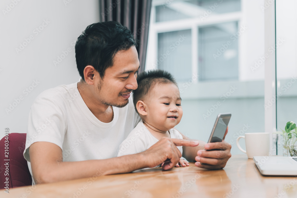 Fototapeta premium Asian father and little son watching video from smartphone at home happiness laughing together, happy family concept.