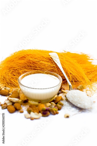 Close up of Raw vermicelli or sevee or seviyan or seviyaan and dry fruits isolated on white with a bowl of milk used to make kheer. photo