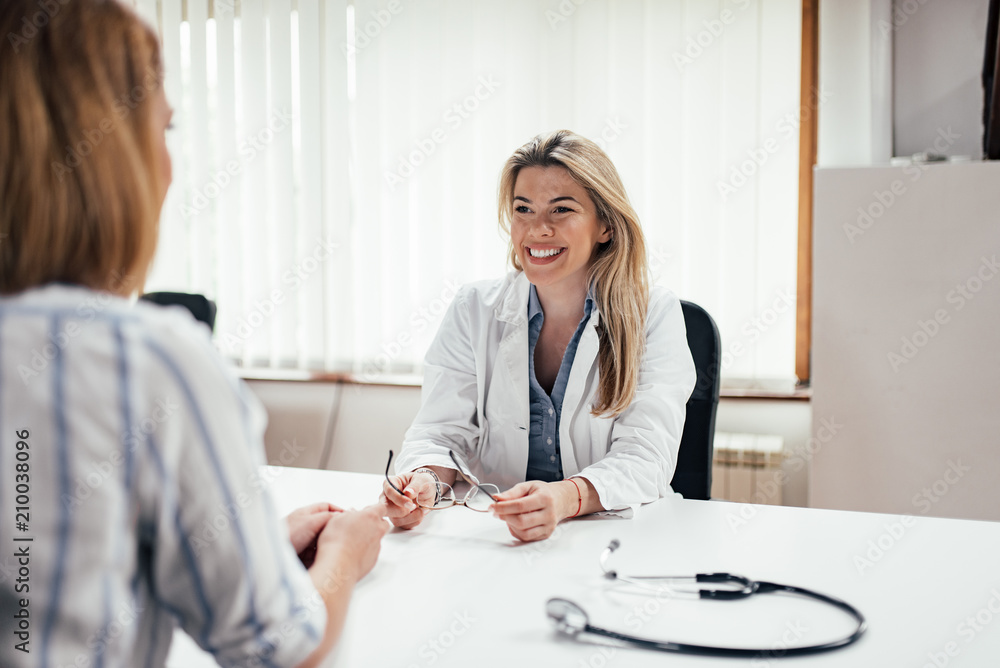 Fototapeta premium Blonde general practitioner holding eyeglasses while talking to a female patient.