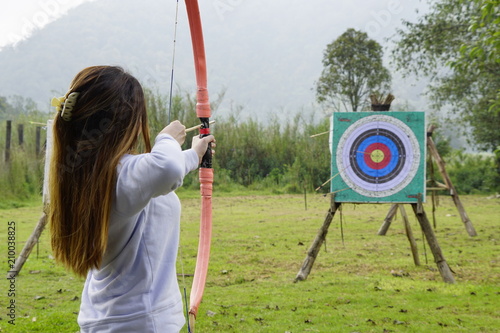 Fotografiet Young woman is aiming in archery  practice n the field with a target in front of her