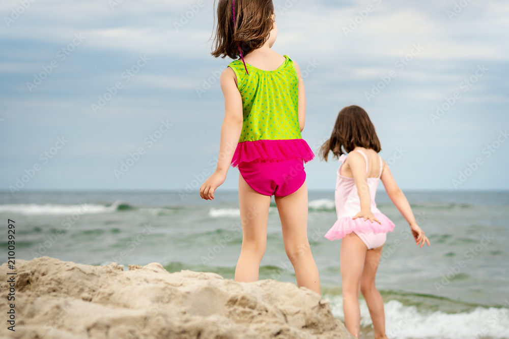 two little girls sisters are standing and playing on the sand at the beach on a summer day