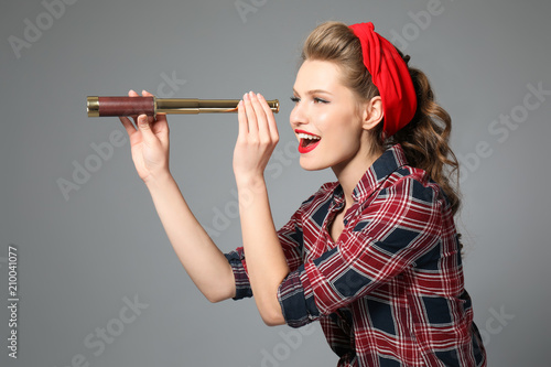фотографія Beautiful young woman looking through spyglass on color background