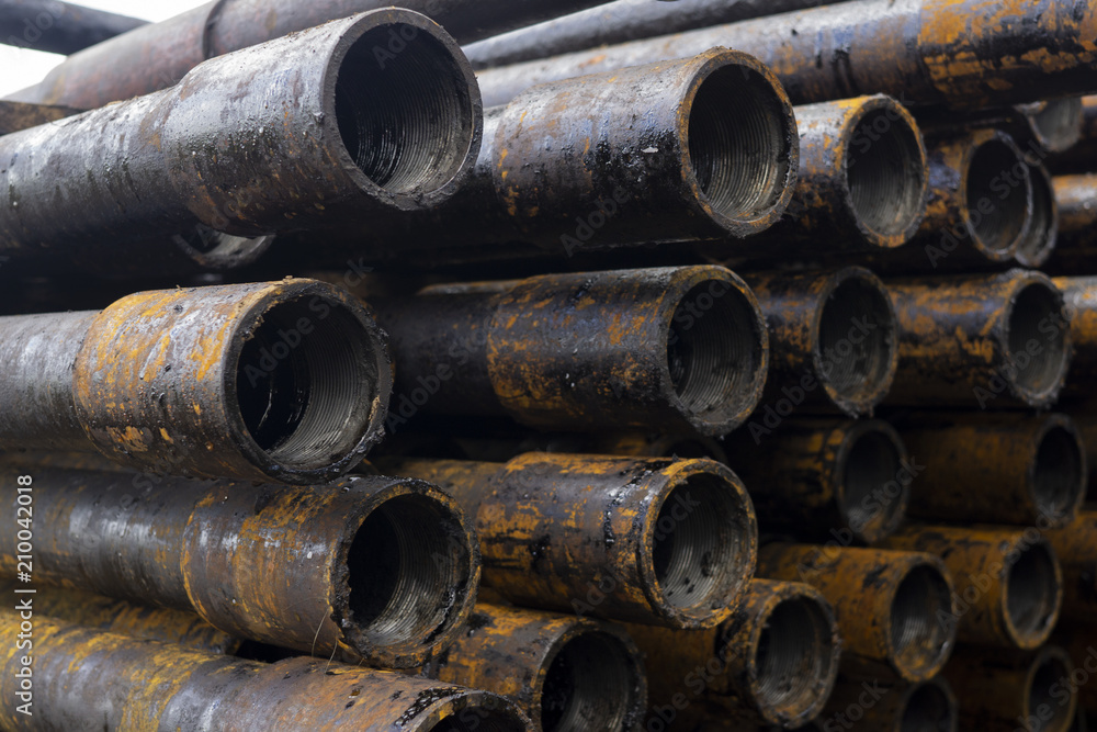 Oil Drill pipe. Rusty drill pipes were drilled in the well section. Downhole drilling rig. Laying the pipe on the deck. View of the shell of drill pipes laid in courtyard of the oil and gas warehouse. Oil Drill pipe. Rusty drill pipes were drilled in the well section. Downhole drilling rig. Laying the pipe on the deck. View of the shell of drill pipes laid in courtyard of the oil and gas warehouse.
