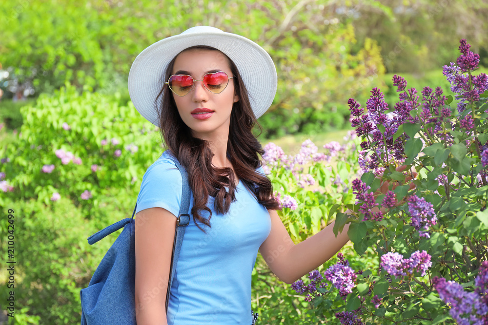 Beautiful young woman wearing hat near blossoming shrub on sunny spring day