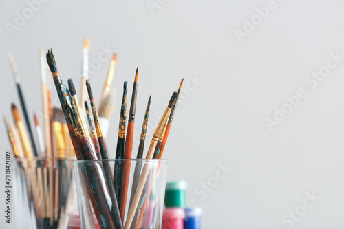 Glass with painting brushes on light background