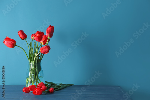 Vase with beautiful tulips on table against color background #210042830