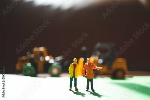 Miniature people, couple engineer standing on construction vehicle background using as logistic and industry concept