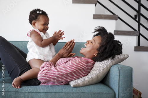 Mother Lying On Sofa At Home Playing Clapping Game With Baby Daughter