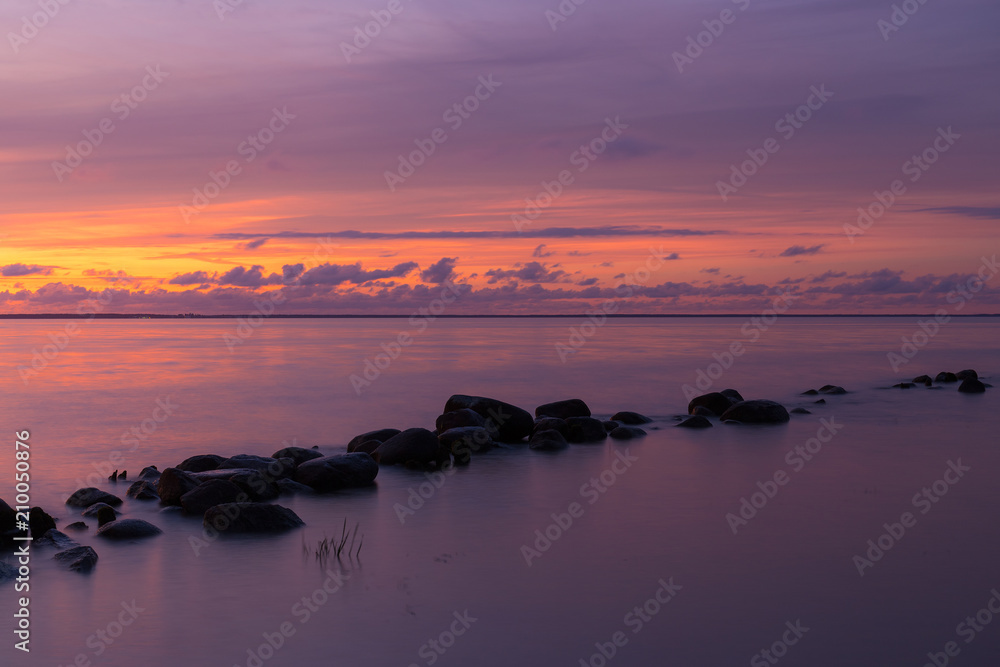Silhouette of the stone breakwater line in the calm water of the sea bay at the evening.