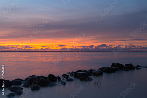 Silhouette of the stone breakwater line in the calm water of the sea bay at the evening.