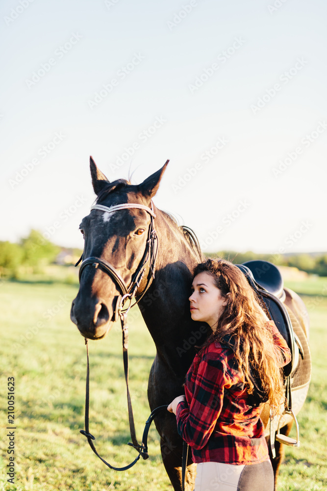 Obraz premium Young girl hugging purebred black horse on the field.