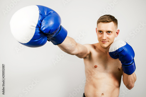 Young man in blue boxing gloves on a light background. © vika33