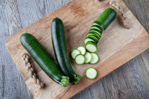 Top view ofTwo Courgettes on a wooden chopping board and another sliced courgette