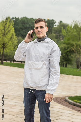 Obraz na płótnie Мужчина в светлой куртке говорит по телефону в парке