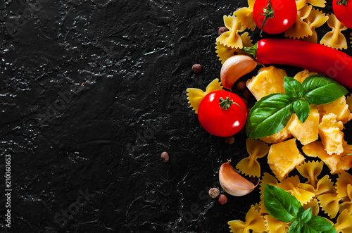 Fototapeta Naklejka Na Ścianę i Meble -  food background. Ingredients for cooking Italian pasta - farfalle pasta, red chili peppers, cherry tomato, basil, black pepper, garlic, parmesan cheese on dark background with copy space. top view