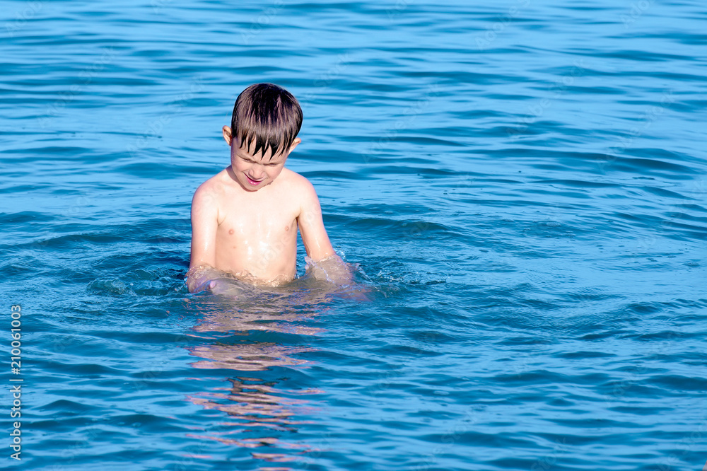 The boy is standing in the sea water on the ocean on a summer day.