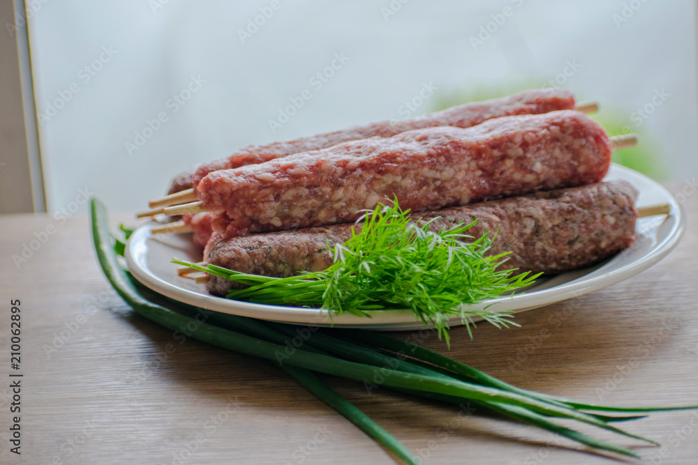 Raw lulya kebab from meat on a white plate with with dill and green onions.