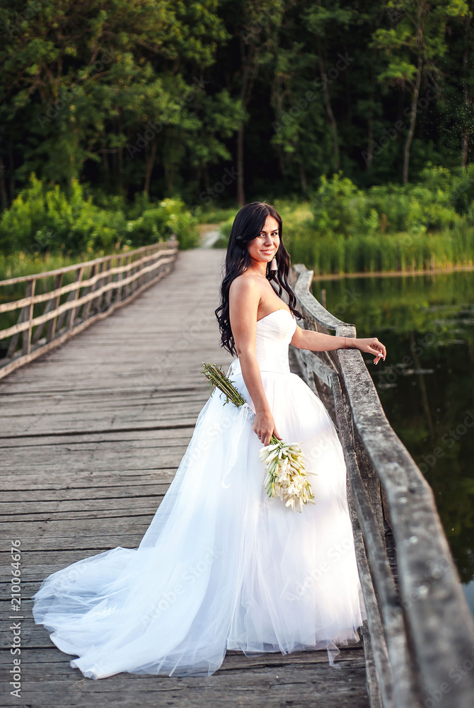 Portrait of a beautiful bride in a white wedding dress in full growth on a wooden bridge Portrait of a beautiful bride in a white wedding dress in full growth on a wooden bridge