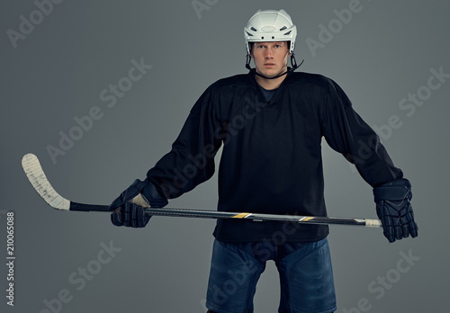 Photography Hockey player wearing black protective gear and white helmet holds a hockey stick on a gray background