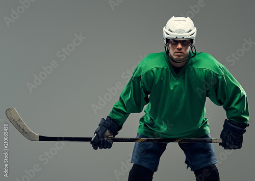 Portrait of a professional hockey player wearing full gear and a hockey stick on a gray background.