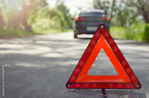 Red triangle emergency stop sign on the road with a broken car behind. Car breakdown concept.