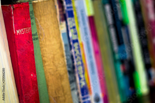 Colorful old hardcover books on a bookshelf. Shot with a shallow depth of field to focus on a mystery novel book with red cover