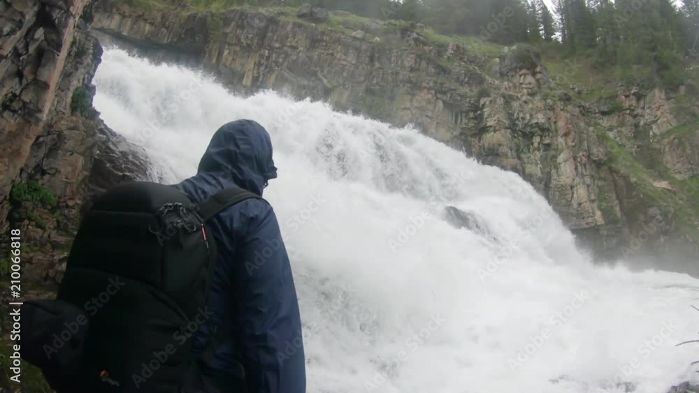 Slow motion of woman hiking towards waterfall as she stops and looks at the raging river. Slow motion of woman hiking towards waterfall as she stops and looks at the raging river.