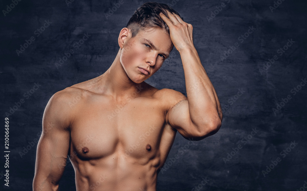 Fototapeta premium Close-up portrait of a sexy shirtless young man model with a muscular body and stylish haircut posing at a studio. Isolated on dark background.