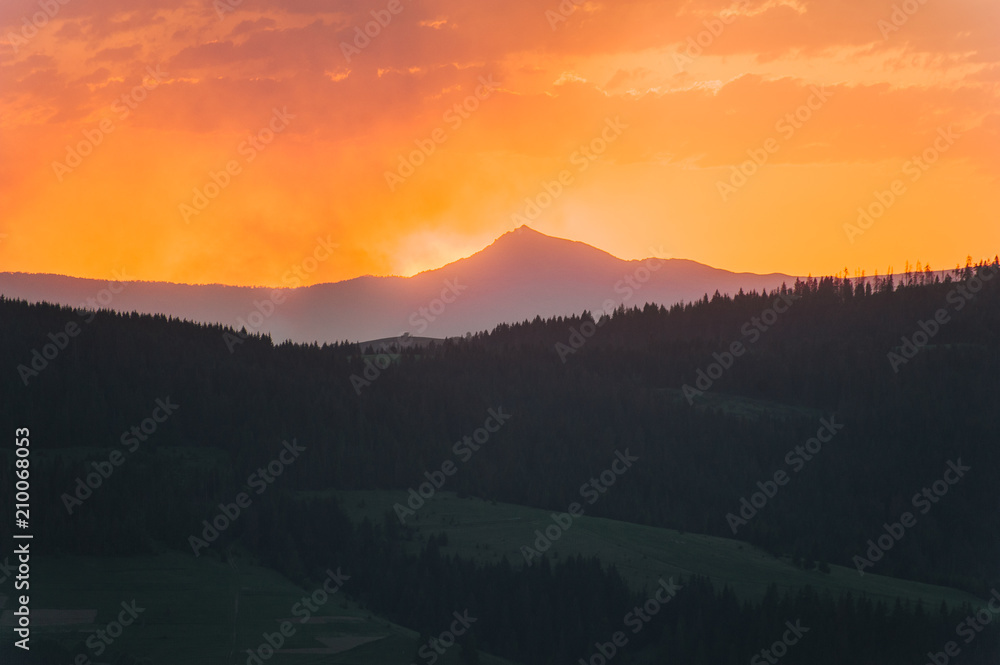 Beautiful dramatic sunrise in the mountains. Landscape with sunlight shining through orange clouds