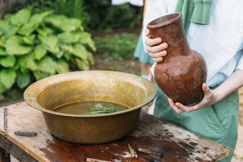 фотографія the boy holds a clay jug, pours water out of it into a copper basin
