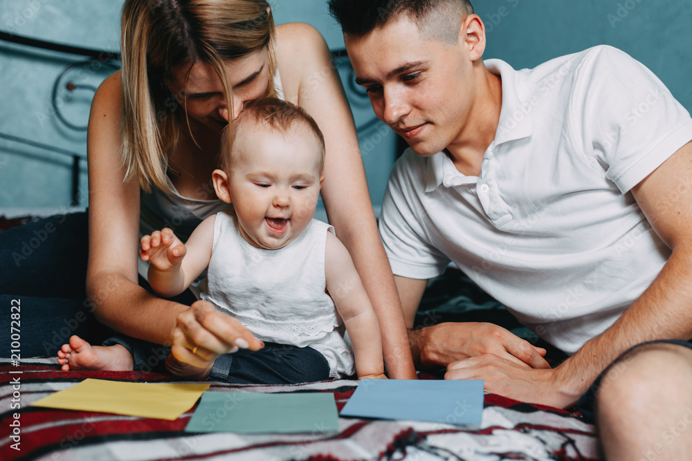 Little child and parents playing colorful training cards and learning the colors sitting together at home bed. Early development, educational play for kids Little child and parents playing colorful training cards and learning the colors sitting together at home bed. Early development, educational play for kids