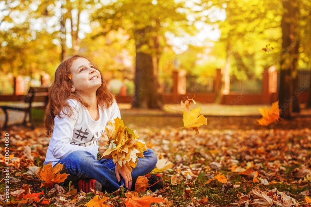 The girl child sits on the grass in the autumn Park with leaves in her hand, dreaming. The girl child sits on the grass in the autumn Park with leaves in her hand, dreaming.