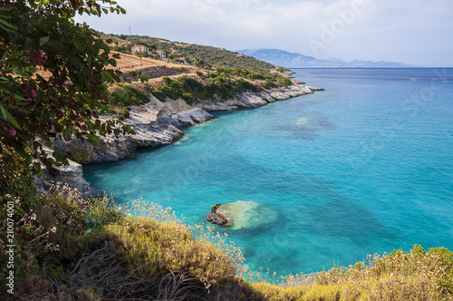 A beautiful summer seascape of bay with crystal turquoise water and rocky coastline with some green flora. Colorful, vacation landscape of greek sea.