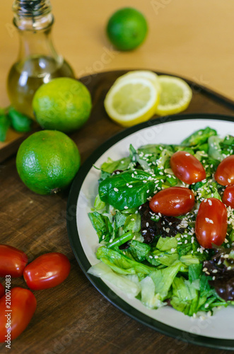 Fresh salad from different kinds of greens and a cherry tomato, dressed with olive oil and sprinkled with sesame seeds