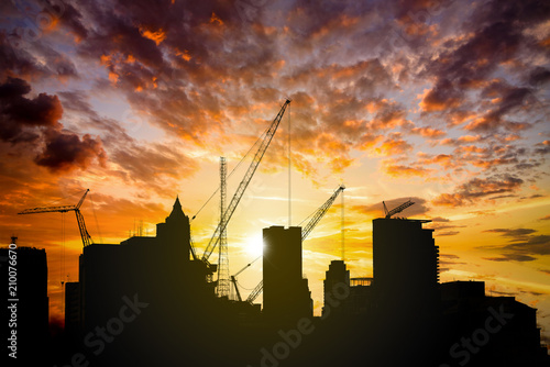Silhouette of crane tower on the construction site with city building background in sunset sky