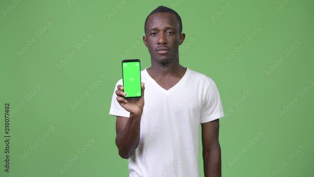 Young African man showing phone against green background Young African man showing phone against green background