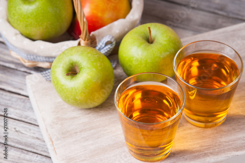 Apple juice in glasses and apples in a wicker basket on wooden table 
