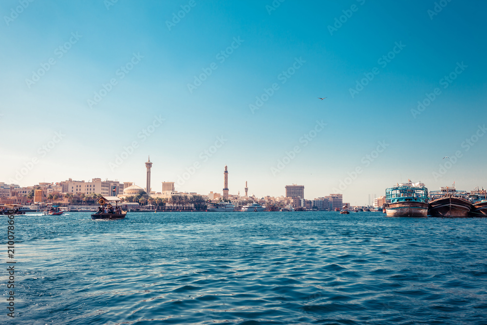 Skyline view of Dubai Creek with traditional boats and piers. Sunny summer day. Famous tourist destination in UAE.