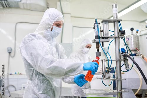 Sports nutrition production worker in protective clothing operating bottle closing machine. 