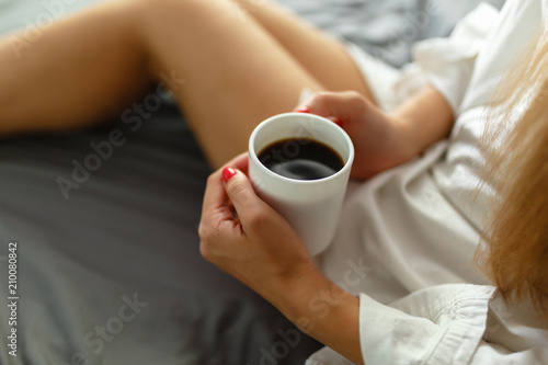 Slim, perfect and beautiful woman drinking her coffee while sitting on bed. Sunny Lazy morning in bed. Cropped image of erotic lying on the bed of a girl in the bedroom. Top view.